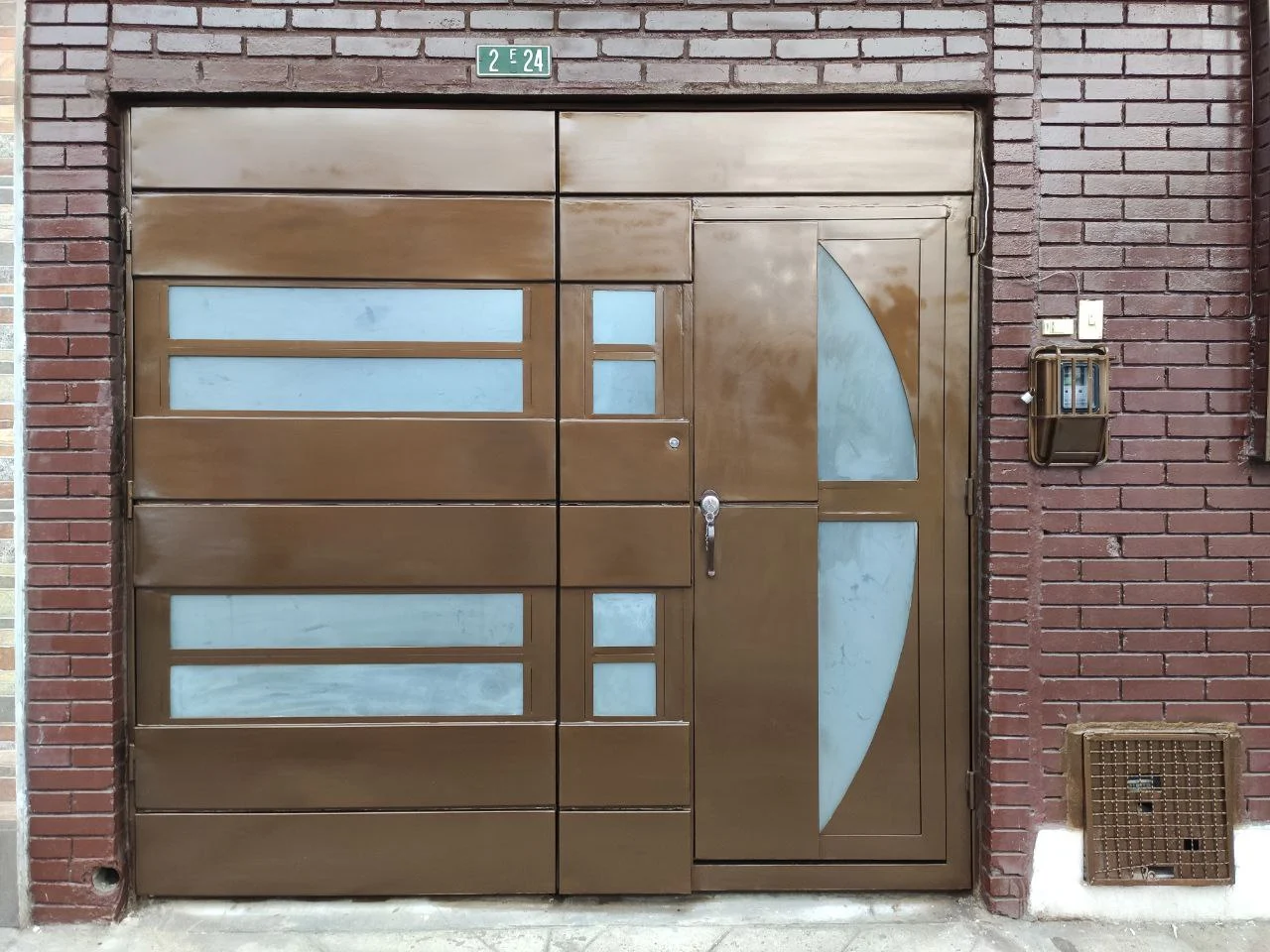 Puerta metálica de acceso principal color bronce con paneles de vidrio