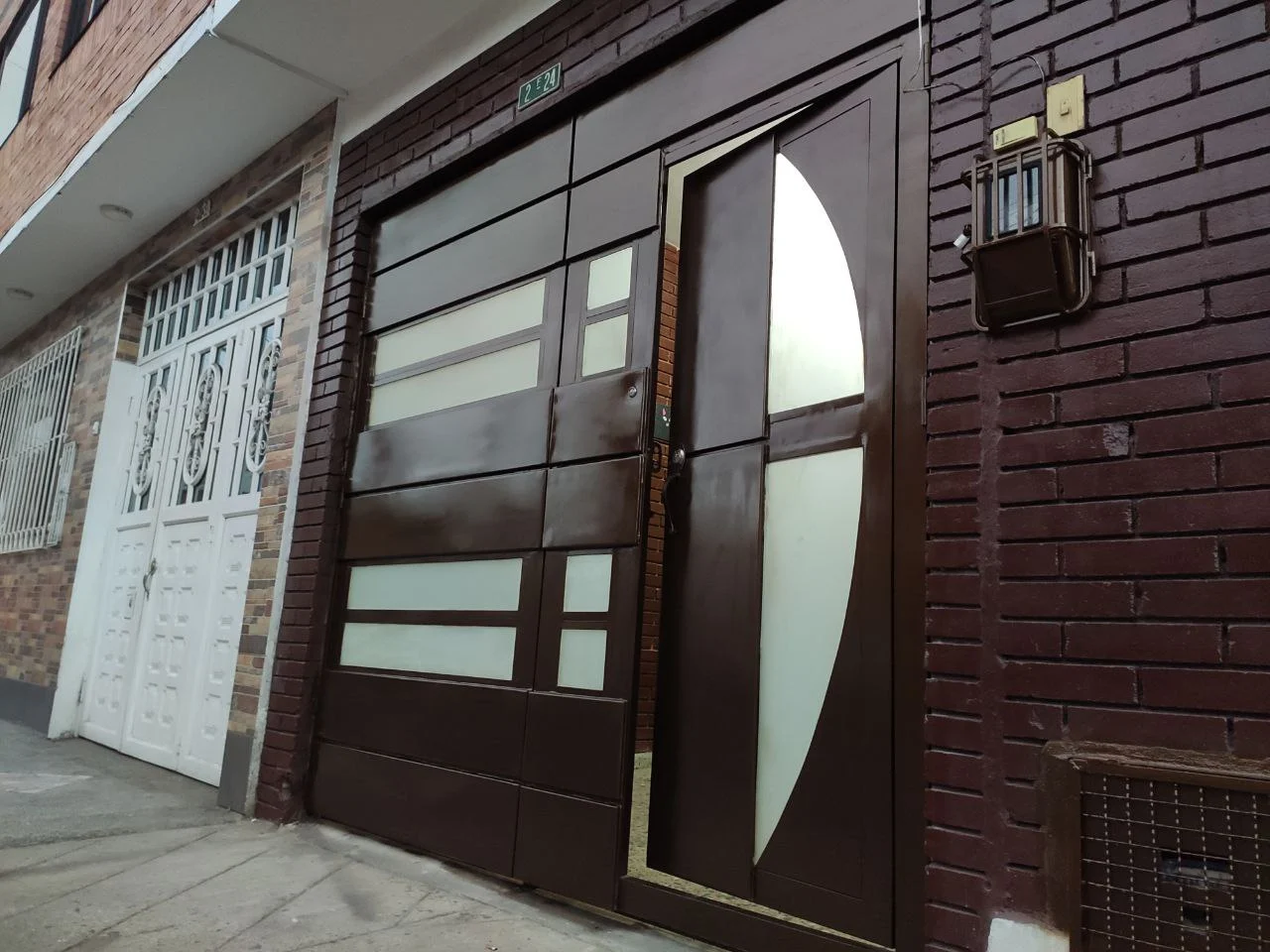 Puerta metálica de acceso con vidrios traslúcidos sobre fachada de ladrillo