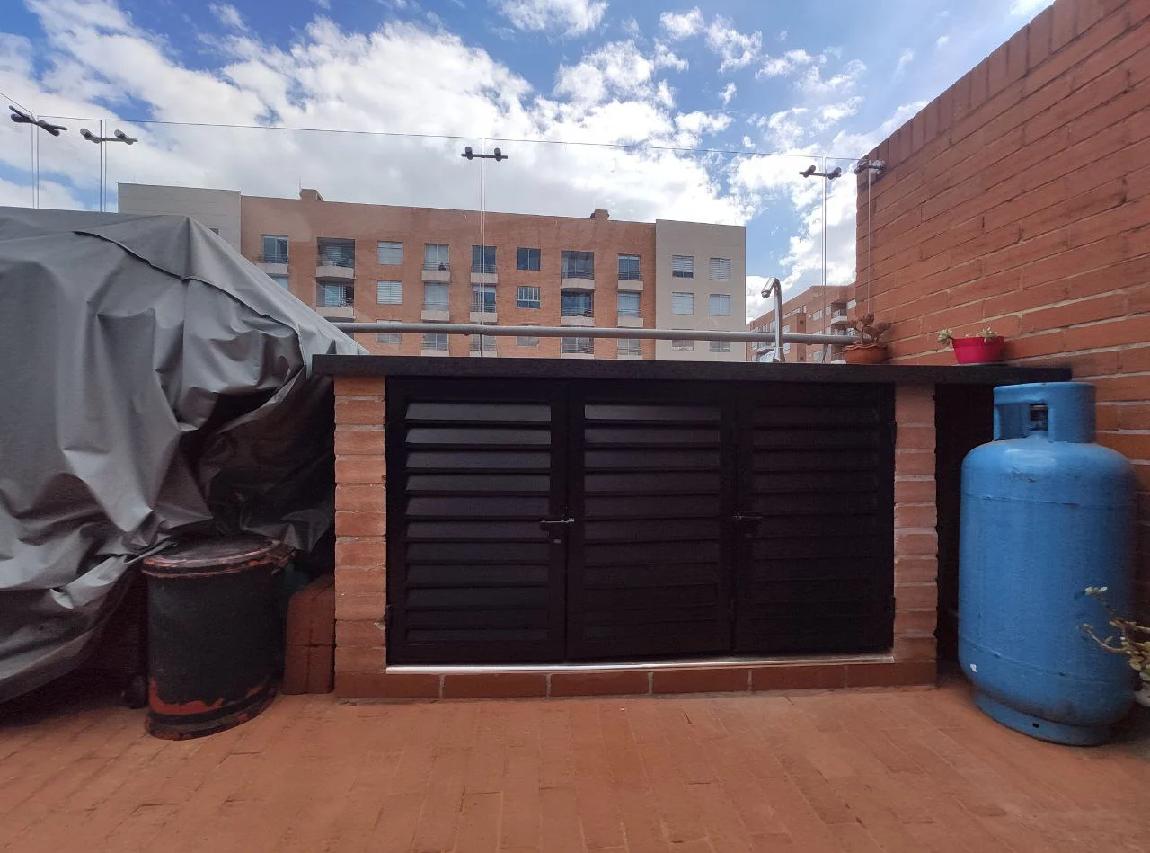 Portón de garaje metálico oscuro instalado sobre fachada de ladrillo a la vista