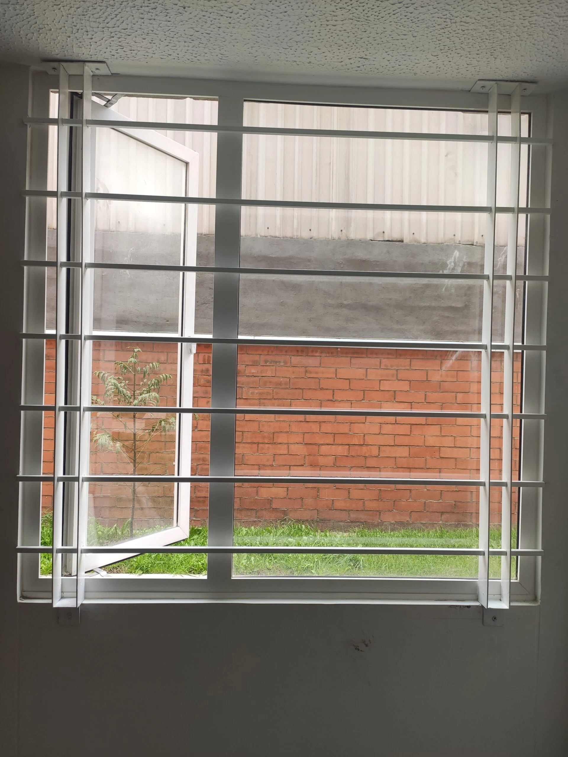 Reja metálica blanca de barrotes horizontales y verticales en ventana