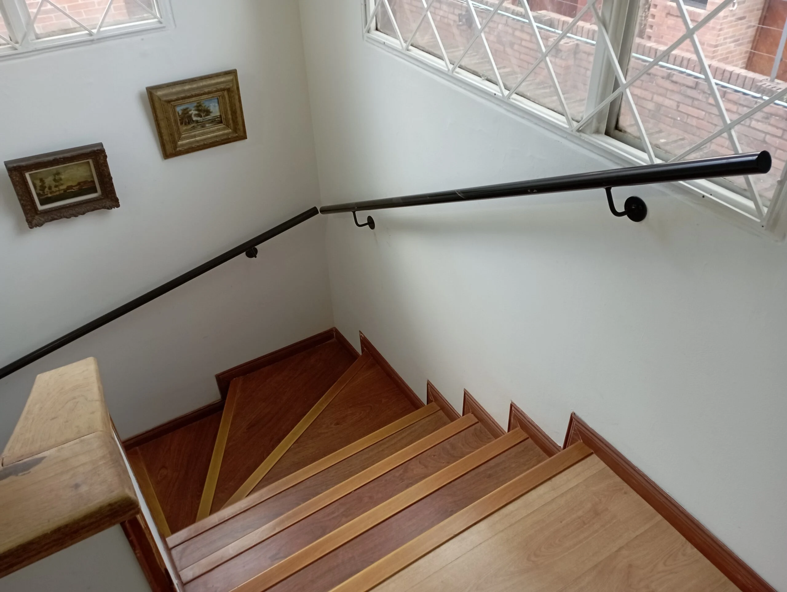 Pasamanos metálico negro anclado a muro en escalera con peldaños de madera