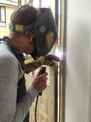 Soldador trabajando en la instalación de puertas metálicas en Bogotá, utilizando equipo de protección y herramientas de metal
