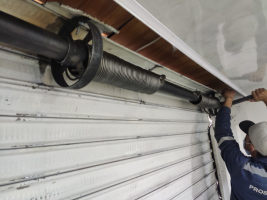 Mantenimiento de cortina metálica enrollable en un espacio interior con sistema de poleas y resortes visibles