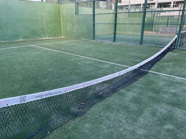Canchas de pádel con red y barandas metálicas en exterior, superficie de césped artificial