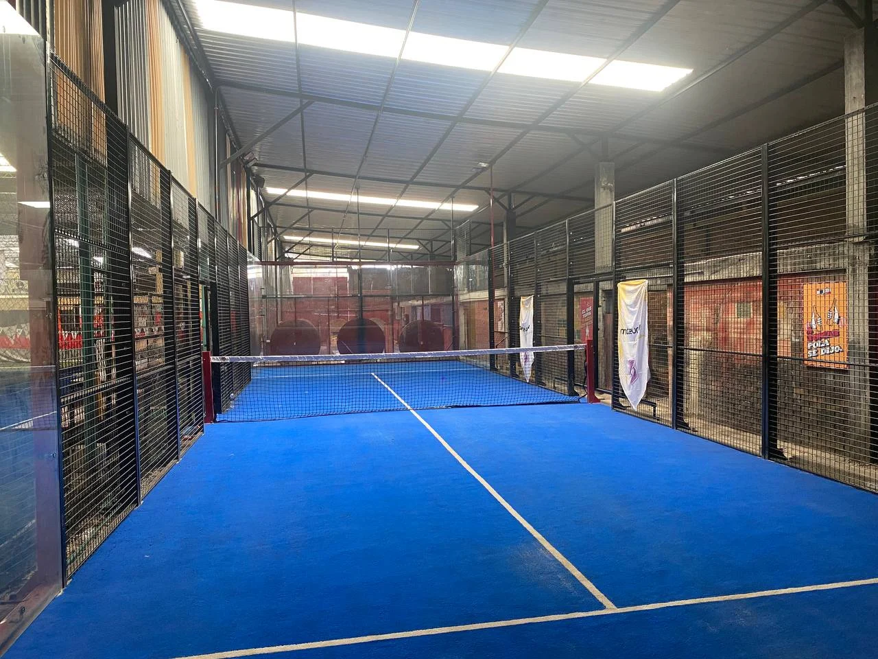 Cancha de pádel interior con piso azul y vidrios en Bogotá