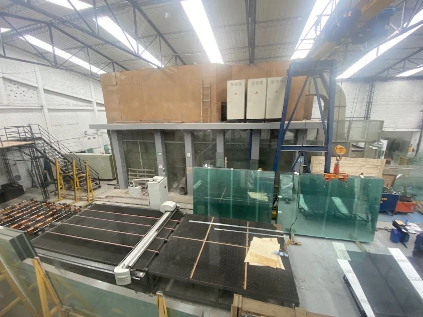 Fábrica de vidrios templados con paneles de vidrio y maquinaria en un entorno industrial interior
