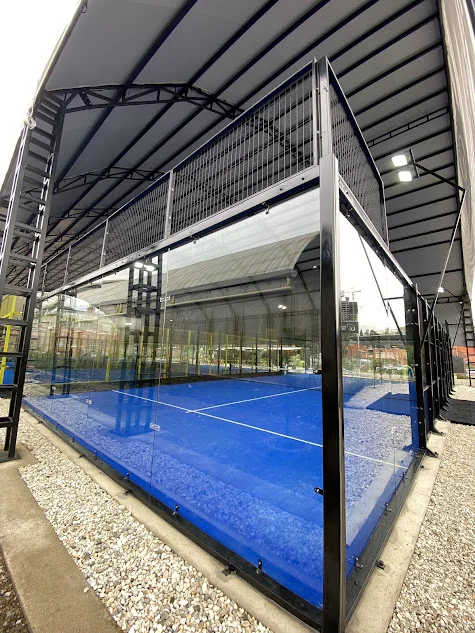 Canchas de pádel con barandas de metal y vidrio en exterior, con superficie azul y estructura metálica