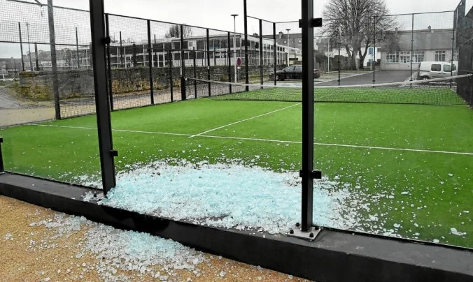 Vidrio roto de una cancha de pádel exterior, con fragmentos de vidrio en el suelo y césped artificial visible