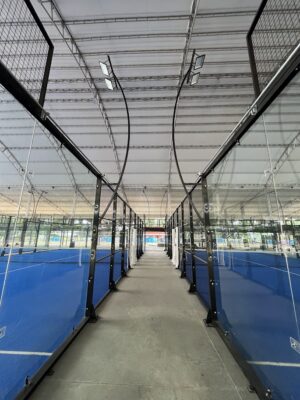Canchas de pádel con barandas de vidrio y estructura de metal en un espacio interior amplio