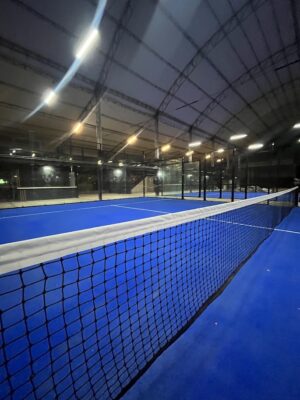 Canchas de pádel interiores con red y superficie azul, bajo estructura metálica y techo cubierto