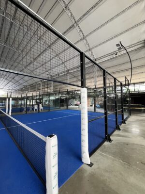 Canchas de pádel interiores con barandas de metal y superficie azul, bajo techo en un espacio cerrado