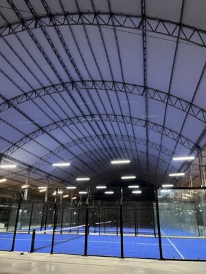 Canchas de pádel con estructura metálica y paneles de vidrio en un interior iluminado