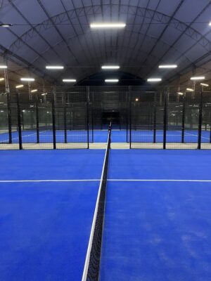 Canchas de pádel interiores con barandas de metal y superficie azul en un recinto techado