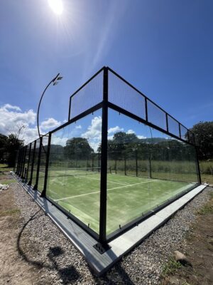 Cancha de pádel exterior con estructura de metal y paneles de vidrio, ubicada en un entorno natural