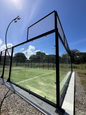 Canchas de pádel exteriores con barandas de metal y paneles de vidrio, rodeadas de césped y naturaleza